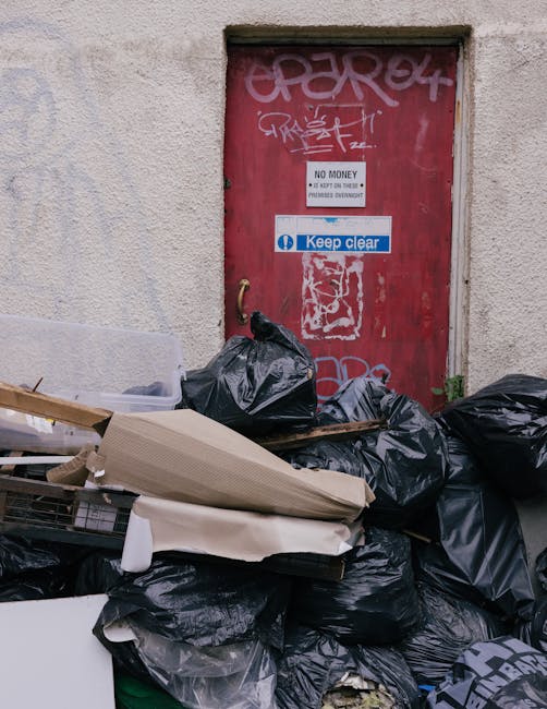 A rectangular white metal sign with black lettering is mounted on a reddish-brown brick wall. The sign displays the message 'NO DUMPING OF RUBBISH,' with the words 'NO DUMPING' positioned above 'OF RU
