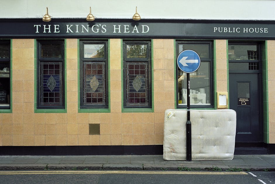 The exterior of a traditional public house named 'The King's Head' displays three tall, narrow windows with decorative stained glass patterns and dark green frames, set into a beige tiled facade with 
