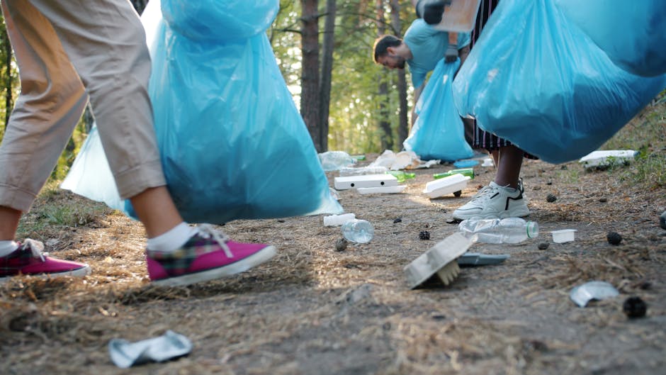 A row of four public waste bins positioned along a paved pathway in an outdoor setting, with each bin designed for different types of rubbish. The first bin from the left is light blue with a rounded,
